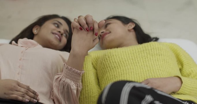 Young Indian sisters and best friends forever lying down on bed as they reenforce their bond and hold strong hands for relationship to strengthen and support each other through high and lows of life