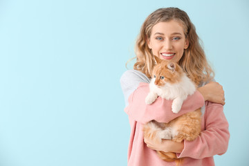 Beautiful young woman with cute cat on color background