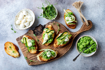 Appetizer crostini with mashed green pea, mozzarella, pea sprouts and zucchini ribbons on wooden...