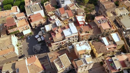 Aerial - slowly tilting down to reveal the cityscape of the resort town located on a mountain; Mediterranean Sea in the background. Taormina, Sicily, southern Italy - Powered by Adobe