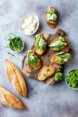 Appetizer crostini with mashed green pea, mozzarella, pea sprouts and zucchini ribbons on wooden board. Delicious healthy snack, spring appetizers