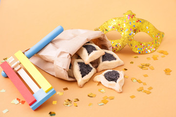 Tasty hamantaschen, gragger and party decor for Purim holiday on color background