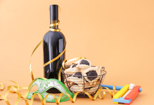 Tasty Hamantaschen, Gragger And Party Decor For Purim Holiday And Bottle Of Wine On Color Background