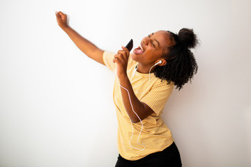 african american woman listening to music with mobile phone and earphones by white background arm raised