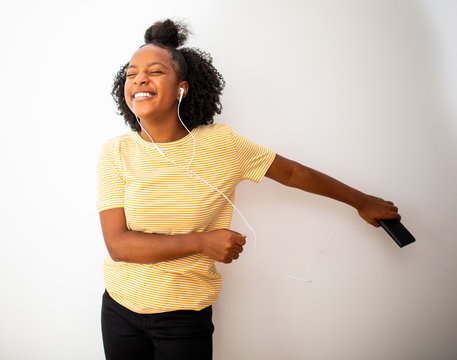 african american teenage girl listening to music with cellphone and earphones against isolated white background and dancing