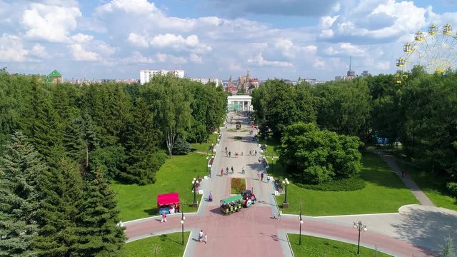 City square in the green park with ferris wheel in summer warm cloudly day. People are walking serenely - Drone Footage