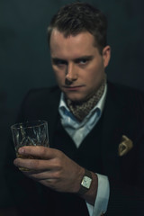 Retro fashion man in dark suit holds a glass of whiskey.