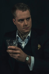 Retro fashion man in dark suit holds a glass of whiskey.