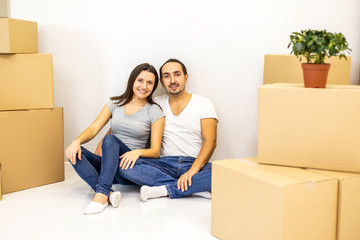 Packed and ready to move in new house. Excited young spouses sitting among carton boxes ready to relocate.