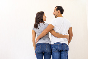 Back view of young couple standing together, embracing, looking at white wall.