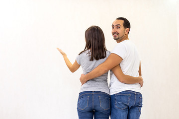 Young couple planning improvements to an apartment standing measuring the height of something against a white wall.