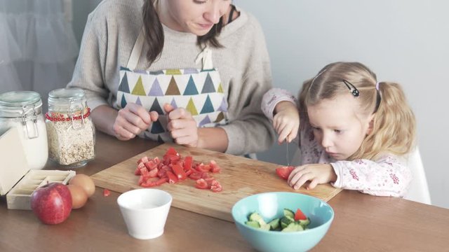 Mom Teaches To Cook A Little Daughter. Girl Tries To Cut Tomato For Salad