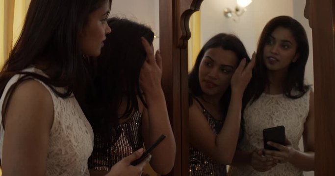 Two young pretty and confident Indian women getting intimate, embracing and taking good looking selfies with each other as they dress in front of mirror at home before heading night-out handheld 60fps