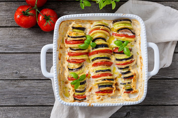 Ratatouille casserole on wooden background. Colorful layers of fresh summer vegetables: zucchini, eggplant, tomatoes on tomato sauce season. Healthy vegan, vegetarian dish. Top view, copy space