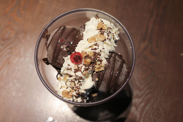 Top view image of Chocolate ice cream in a bowl with whipped cream.Hand holding a red cherry and put it on the top of chocolate ice cream bowl.