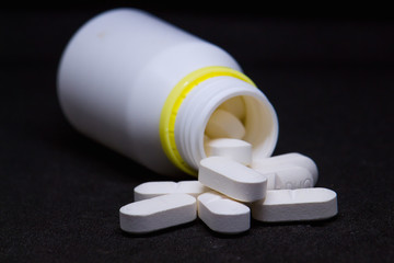 jar with white pills on black background - closeup