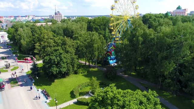 City square in the green park with ferris wheel in summer warm cloudly day. People are walking serenely - Drone Footage