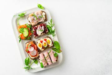 Selection of Danish smorrebrod open sandwiches on a platter on white background, horizontal...