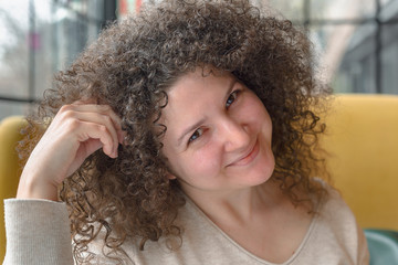 Young woman with curly hair looks cheerful in a cafe