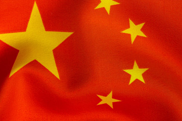 Chinese flag. Flag of the People's Republic of China with yellow stars on a red background. Chinese flag with silk folds in the wind and a textile and fabric texture