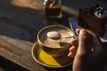 man hand use spoon mix coffee and sugar in the morning. cake and coffee on the wood table.