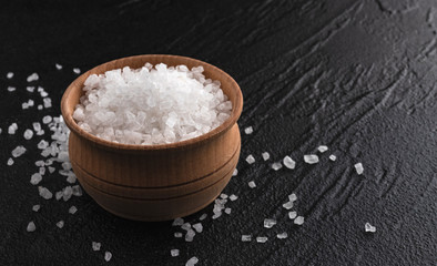 Sea salt in wooden bowl on black background