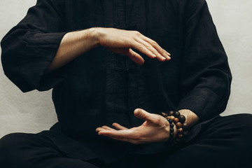 A man in black shirt sitting and doing qigong. Hands direct energy. Prayer, gratitude.Practicing monk. Qi energy. Yoga pose. Close up - obrazy, fototapety, plakaty