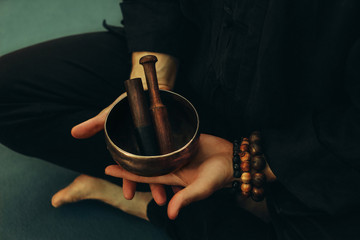 Top view of two hands of a man holding a singing bowl with sticks in front of him. Listen to the healing vibrations of Tibetan bowls. Humility and calm. Rosary on the hand. Close-up