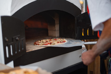 Baker puts the fresh pizza in the oven