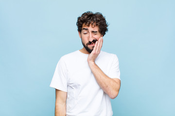young crazy bearded man holding cheek and suffering painful toothache, feeling ill, miserable and...