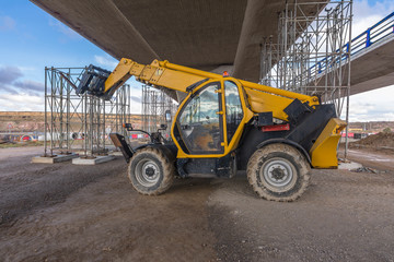 Telehandler on a construction site, preparing to raise construction parts