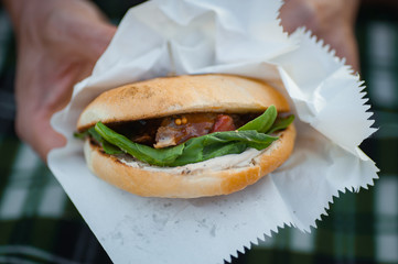 Street food. Burger with spinach, strawberries and duck in paper cover. Men's hands hold a burger