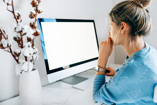Side view of freelacer businesswoman using desktop computer in creative office. Photo of young blonde woman sit indoors at home working on computer with blank screen for your text message or content