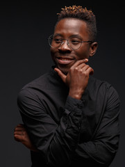 Emotional portrait of a young African man in black clothing against a dark background. Studio photography.