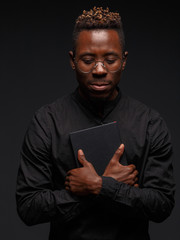 A young African man in black clothes on a dark background holds in the hands of a book.