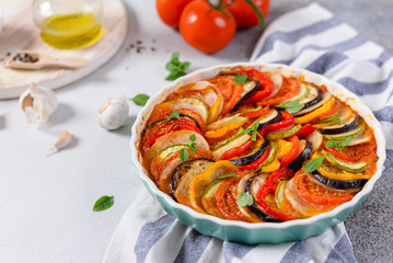 Ratatouille casserole on white background. Colorful layers of fresh summer vegetables: zucchini, eggplant, tomatoes and potatoes. Healthy vegan, vegetarian dish. Side view, copy space. Menu, recipe
