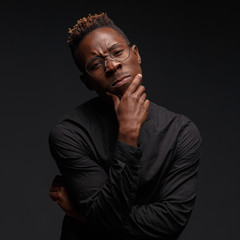 Emotional portrait of a young African man in black clothing against a dark background. Studio photography.