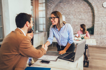 Young couple signing a contract  on a meeting with investment agent in the office. Shaking hands after signing documents.