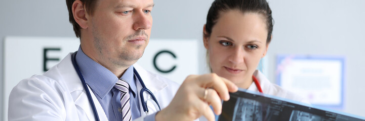 Portrait of surgeons in white medical gowns looking carefully at roentgenogram of patient. Doctors...