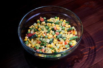 Frozen different vegetables in a glass plate on a wooden background.