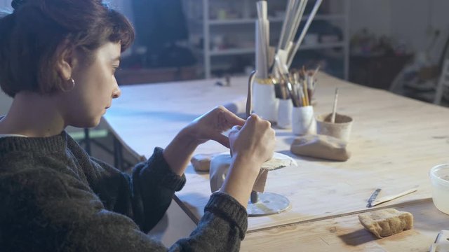 Pottery woman creating clay cuo. Working in her workshop at the evening time.
