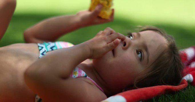 Cute little girl child putting finger in nose while lying outside in nature