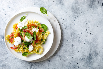 Italian pasta mafalde with green peas, prosciutto, burrata,  and spinach