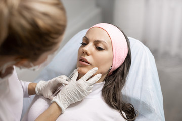 Permanent makeup, tattooing of lips. Cosmetologist in white gloves applying make up for woman in beauty salon