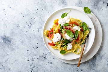 Italian pasta mafalde with green peas, prosciutto, burrata,  and spinach