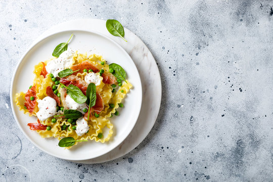 Italian pasta mafalde with green peas, prosciutto, burrata,  and spinach