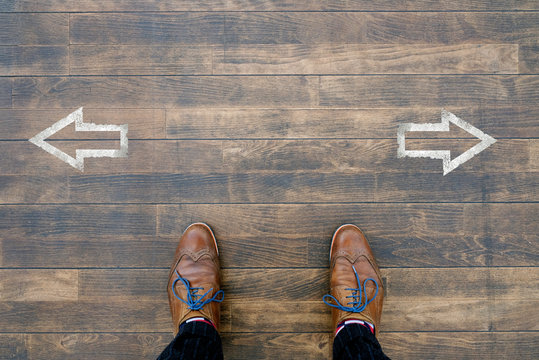 Man Looking Down At Two Arrows Pointing In Opposite Directions