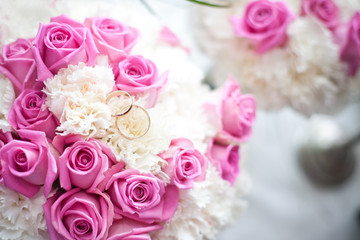 Bride wedding bouquet. Golden rings on top of pink roses background. Ceremony jewelry symbol of love.