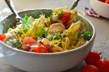 Vegan Bowl. Vegetable salad with avocado, tomatoes, herbs, iceberg lettuce, lettuce, sweet and sour sauce and yogurt. Healthy vegetarian lunch. Salad in a gray clay bowl on a gray concrete background.