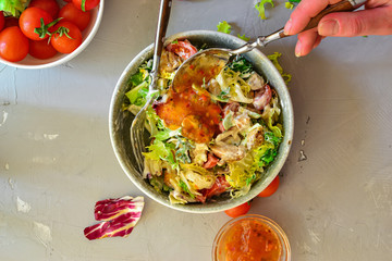 Vegan Bowl. Vegetable salad with avocado, tomatoes, herbs, iceberg lettuce, lettuce, sweet and sour sauce and yogurt. Healthy vegetarian lunch. Salad in a gray clay bowl on a gray concrete background.